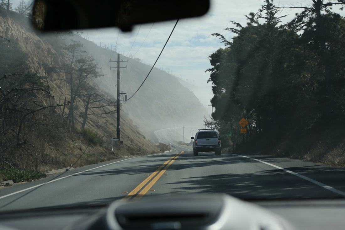 a car driving down a road next to a lush green hillside