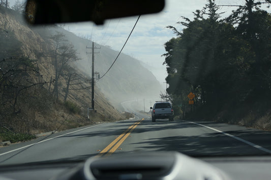 a car driving down a road next to a lush green hillside